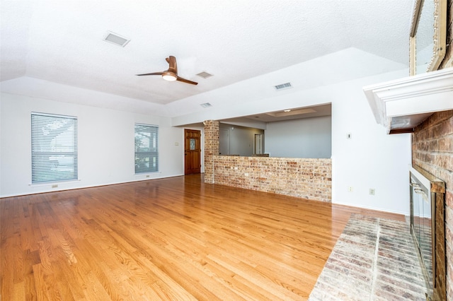 unfurnished living room featuring a fireplace, wood-type flooring, a textured ceiling, and ceiling fan