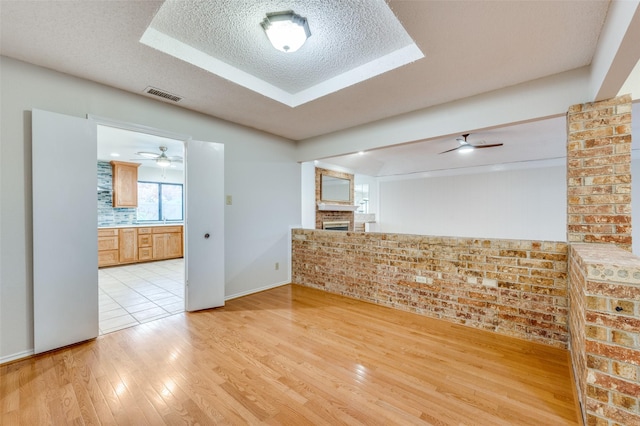 spare room featuring brick wall, a textured ceiling, ceiling fan, light hardwood / wood-style flooring, and a fireplace