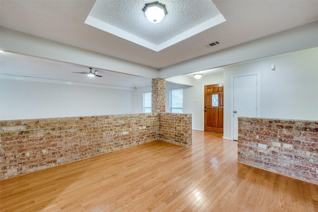 unfurnished room featuring ornate columns, brick wall, ceiling fan, light hardwood / wood-style floors, and a textured ceiling