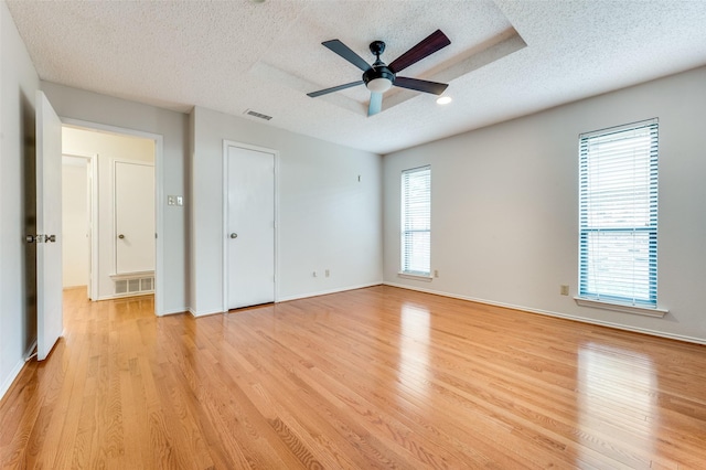 interior space with a raised ceiling, ceiling fan, a textured ceiling, and light wood-type flooring