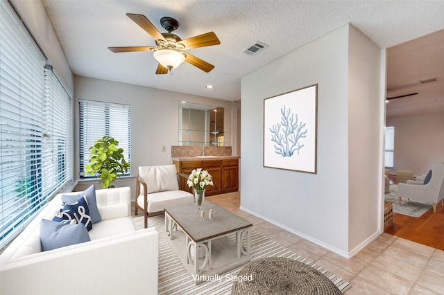 tiled living room with ceiling fan, a healthy amount of sunlight, sink, and a textured ceiling