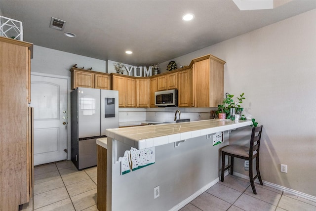 kitchen featuring light tile patterned floors, appliances with stainless steel finishes, tile counters, a kitchen bar, and kitchen peninsula