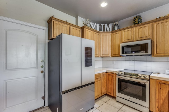 kitchen featuring stainless steel appliances, tile counters, backsplash, and light tile patterned floors