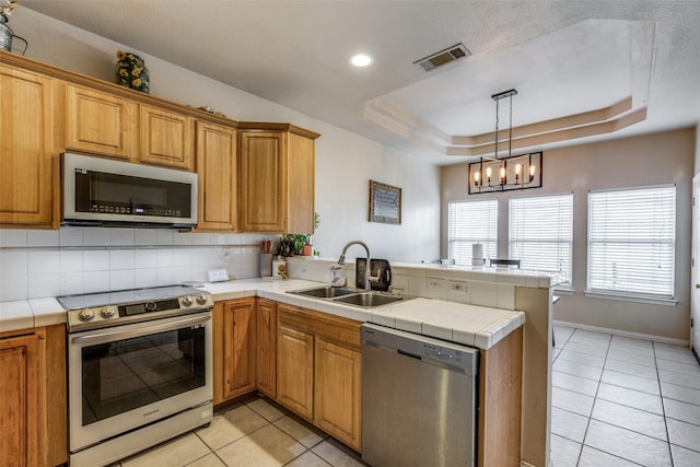 kitchen featuring sink, tile counters, a tray ceiling, kitchen peninsula, and stainless steel appliances