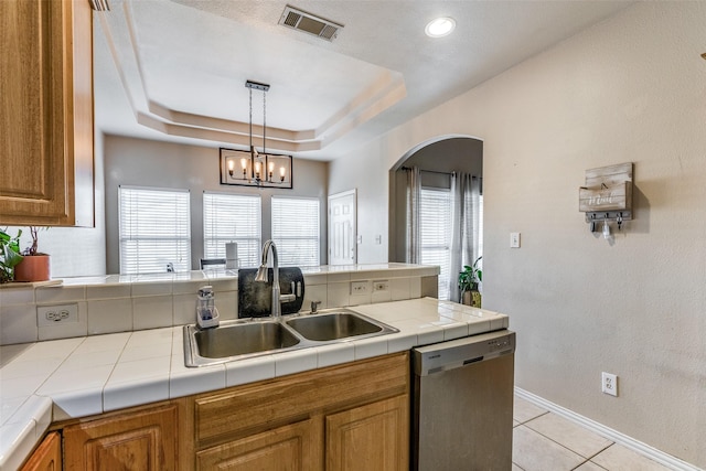 kitchen with a raised ceiling, dishwasher, sink, and tile counters