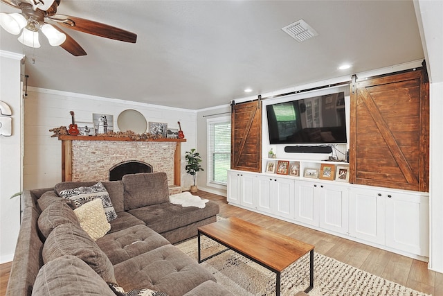 living room with light wood-type flooring, a barn door, a stone fireplace, and crown molding