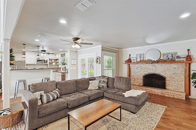 living room featuring ceiling fan, ornamental molding, a textured ceiling, a fireplace, and light hardwood / wood-style floors