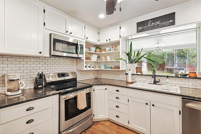 kitchen with white cabinets, stainless steel appliances, dark stone counters, and sink