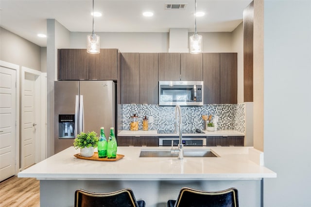 kitchen featuring pendant lighting, a breakfast bar, appliances with stainless steel finishes, and light hardwood / wood-style flooring