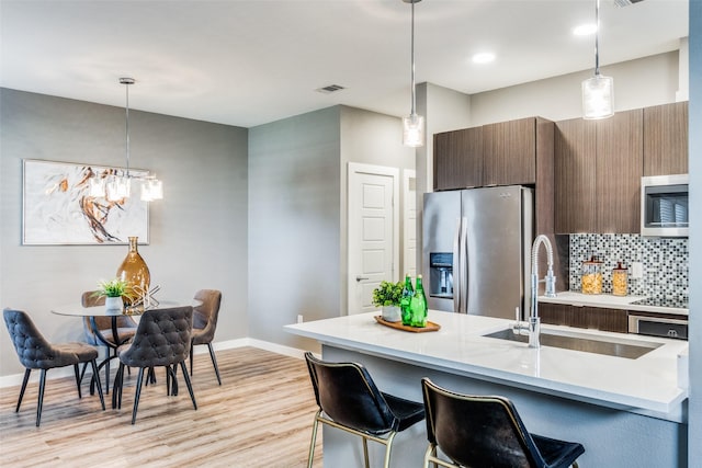 kitchen with pendant lighting, backsplash, sink, light wood-type flooring, and stainless steel appliances