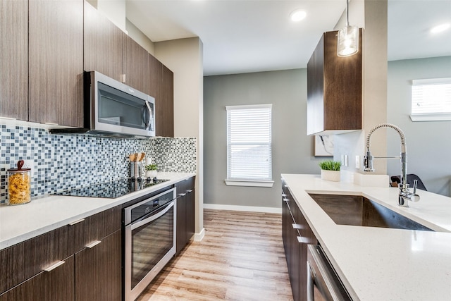 kitchen with sink, hanging light fixtures, decorative backsplash, appliances with stainless steel finishes, and light hardwood / wood-style floors