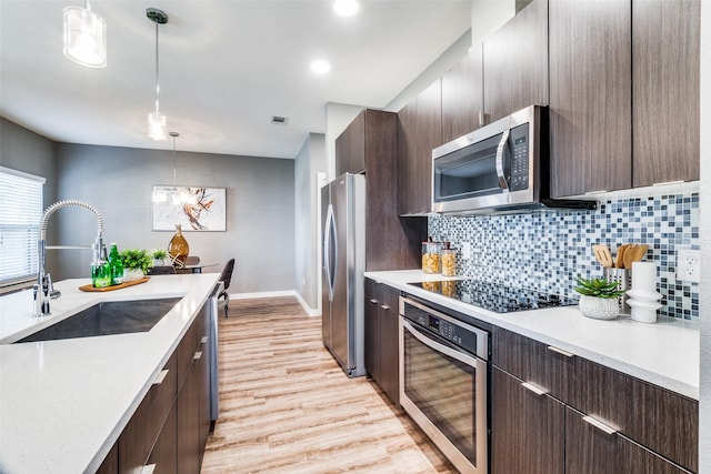 kitchen with sink, hanging light fixtures, stainless steel appliances, decorative backsplash, and light wood-type flooring