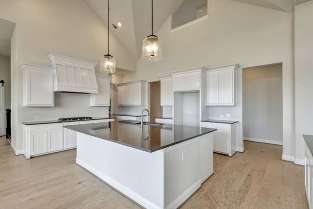 kitchen with sink, high vaulted ceiling, an island with sink, pendant lighting, and white cabinets