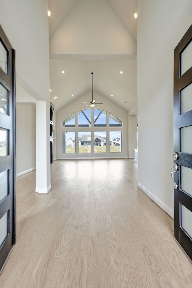 unfurnished living room featuring ceiling fan, high vaulted ceiling, and light wood-type flooring