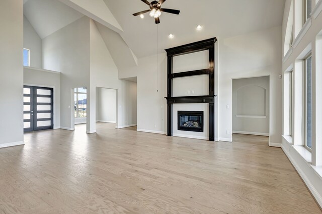 unfurnished living room with ceiling fan, light wood-type flooring, high vaulted ceiling, and french doors