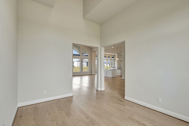 spare room featuring a towering ceiling and light hardwood / wood-style flooring