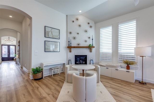 living area with french doors, light hardwood / wood-style flooring, vaulted ceiling, and a healthy amount of sunlight