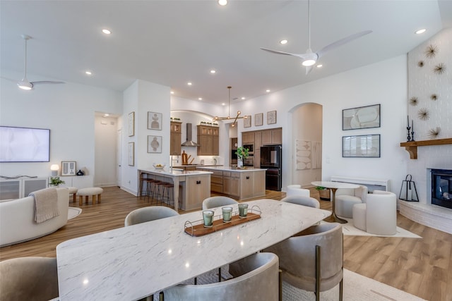 dining area with a fireplace, ceiling fan with notable chandelier, and light hardwood / wood-style flooring