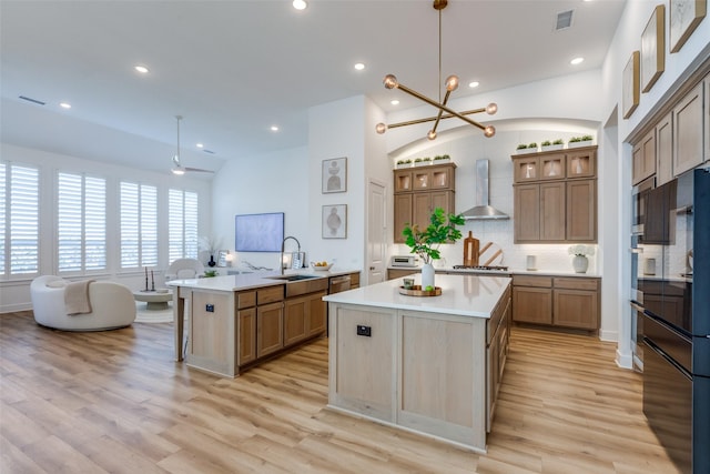 kitchen with a center island, wall chimney range hood, sink, hanging light fixtures, and kitchen peninsula