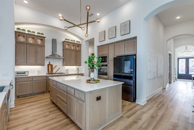 kitchen featuring appliances with stainless steel finishes, wall chimney exhaust hood, light hardwood / wood-style flooring, an inviting chandelier, and a kitchen island