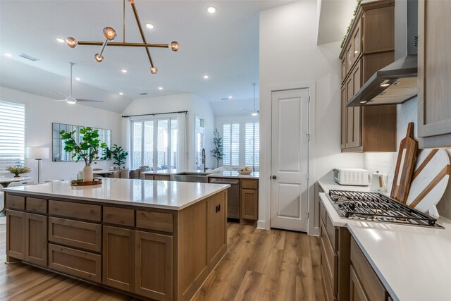 kitchen with dishwasher, wall chimney range hood, lofted ceiling, a kitchen island, and light wood-type flooring