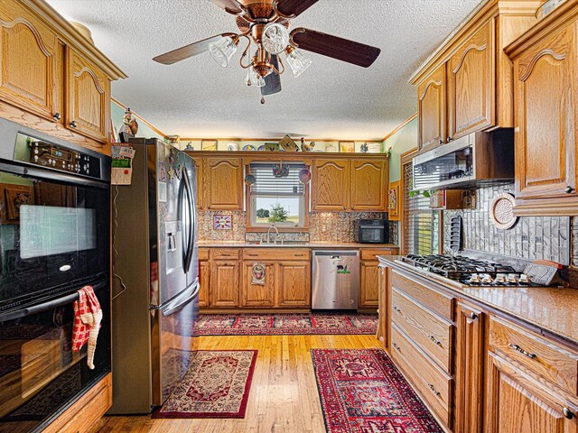 kitchen with sink, tasteful backsplash, a textured ceiling, light wood-type flooring, and black appliances