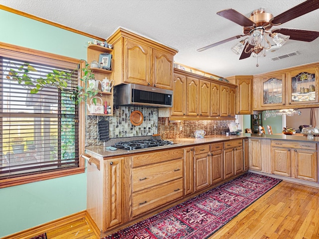 kitchen with appliances with stainless steel finishes, decorative backsplash, ceiling fan, a textured ceiling, and light hardwood / wood-style flooring