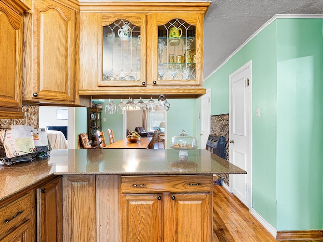 kitchen with ornamental molding, kitchen peninsula, a textured ceiling, and light wood-type flooring