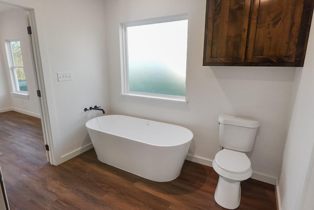 bathroom with a tub to relax in, plenty of natural light, wood-type flooring, and toilet