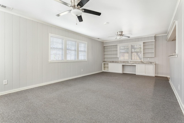 unfurnished living room featuring wooden walls, ceiling fan, crown molding, and a wealth of natural light