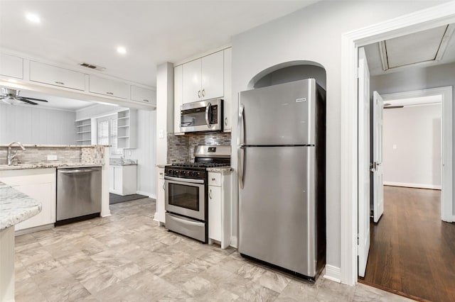 kitchen featuring white cabinetry, ceiling fan, light stone countertops, decorative backsplash, and appliances with stainless steel finishes