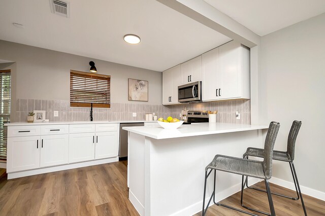 kitchen featuring a breakfast bar, white cabinets, light hardwood / wood-style flooring, kitchen peninsula, and stainless steel appliances