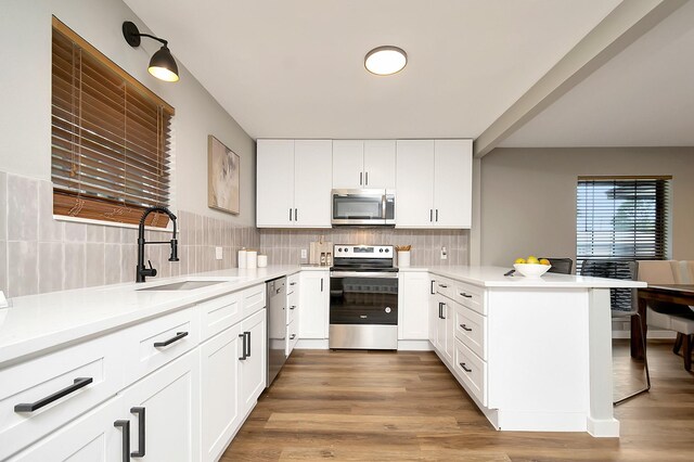 kitchen featuring kitchen peninsula, stainless steel appliances, white cabinetry, and light hardwood / wood-style floors