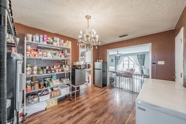 kitchen featuring hanging light fixtures, an inviting chandelier, stainless steel fridge, hardwood / wood-style floors, and a textured ceiling