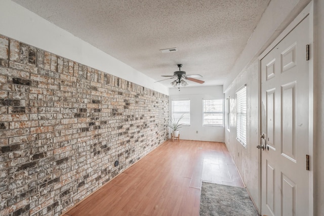 interior space with ceiling fan, light hardwood / wood-style floors, a textured ceiling, and brick wall