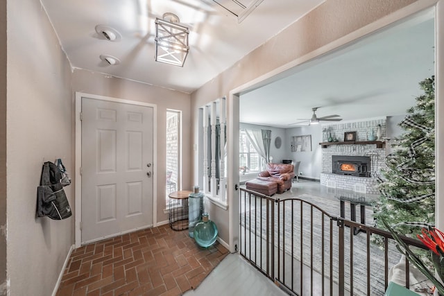 foyer featuring ceiling fan and a brick fireplace