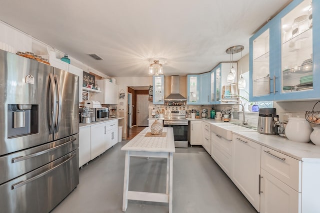 kitchen with sink, wall chimney exhaust hood, decorative light fixtures, white cabinetry, and stainless steel appliances