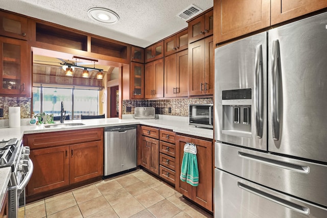 kitchen featuring backsplash, sink, a textured ceiling, light tile patterned flooring, and stainless steel appliances