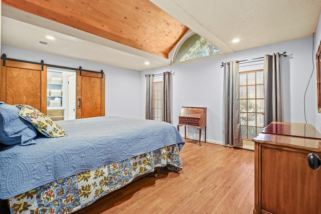 bedroom featuring a barn door, light hardwood / wood-style flooring, and lofted ceiling