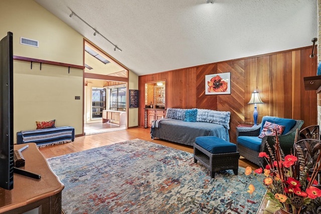 living room with wood walls, light wood-type flooring, a textured ceiling, and high vaulted ceiling