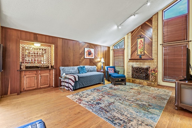 living room with a textured ceiling, light hardwood / wood-style flooring, lofted ceiling, and wood walls