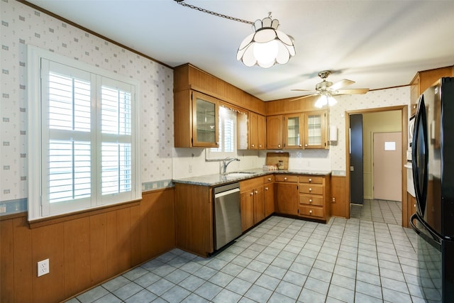 kitchen featuring black refrigerator, dishwasher, sink, ornamental molding, and wooden walls