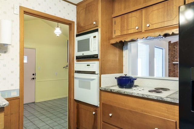 kitchen with white appliances, light tile patterned floors, hanging light fixtures, and light stone counters