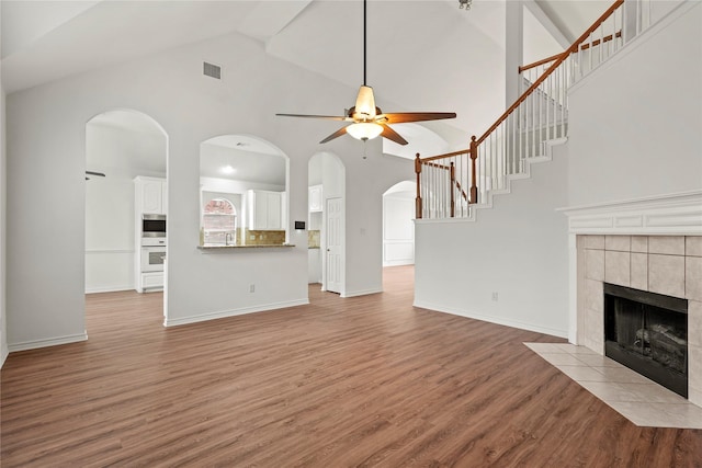 unfurnished living room with light wood-type flooring, high vaulted ceiling, ceiling fan, and a tiled fireplace