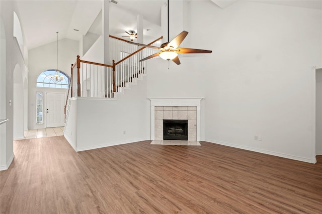 unfurnished living room featuring hardwood / wood-style floors, ceiling fan with notable chandelier, high vaulted ceiling, and a tiled fireplace