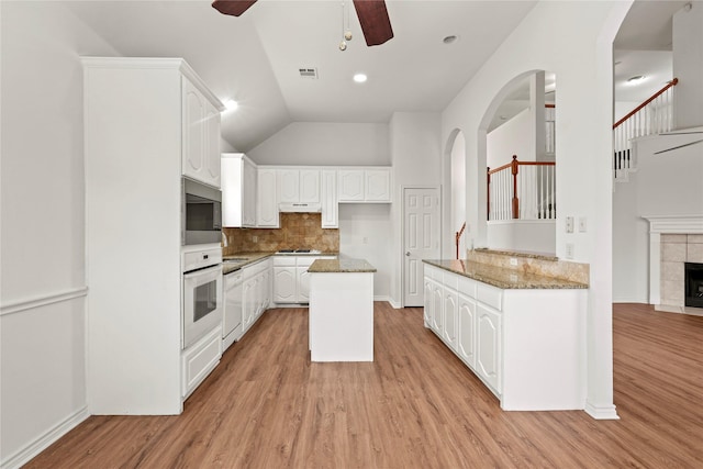 kitchen with white cabinets, light hardwood / wood-style floors, light stone counters, and a tiled fireplace