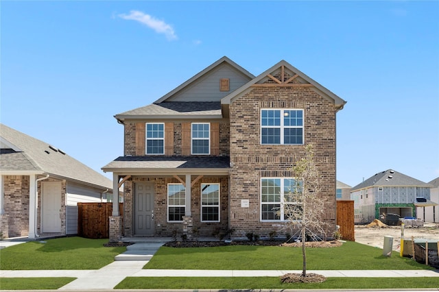 view of front of house featuring brick siding, roof with shingles, a front yard, and fence