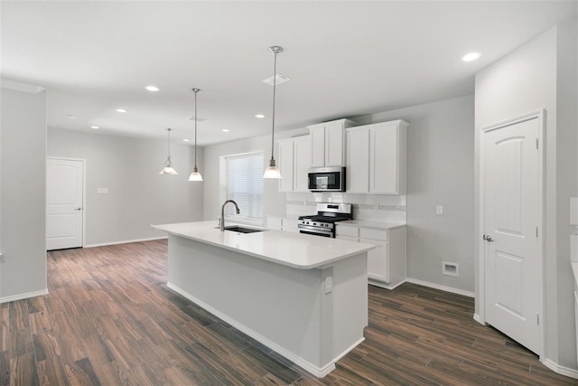 kitchen with stainless steel appliances, sink, decorative light fixtures, white cabinetry, and an island with sink