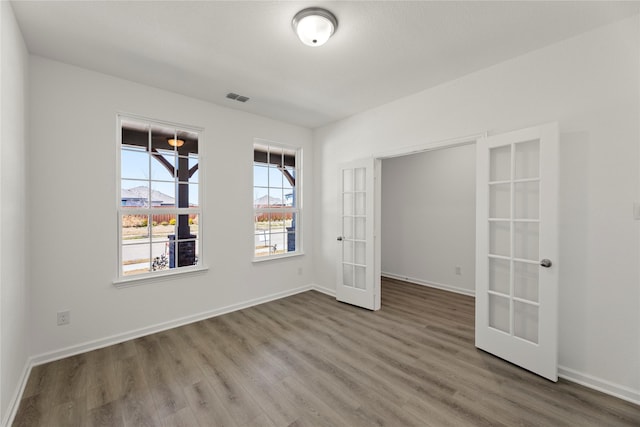 unfurnished room with wood finished floors, french doors, visible vents, and baseboards