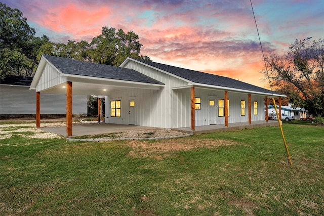 back house at dusk featuring a carport and a lawn